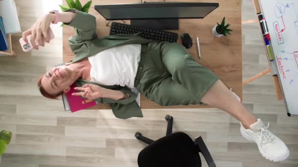 mosolygós nő csinál szelfi, miközben feküdt az asztalon az ebédszünetben az irodában, felülnézet - Felvétel, videó