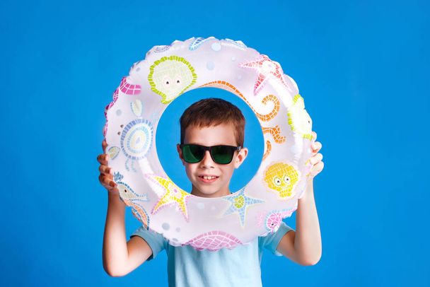 boy holding inflatable ring both hands in swimming pool on light blue studio background - Photo, Image