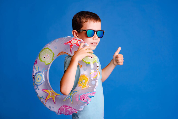мальчик наслаждается бассейном с большим пальцем вверх в синей футболке на светло-голубом студийном фоне - Фото, изображение