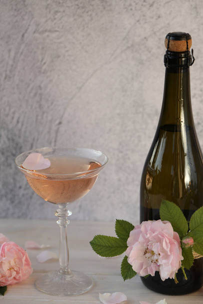ライトグレーの背景にバラの花が付いたピンクのシャンパンガラス - 写真・画像
