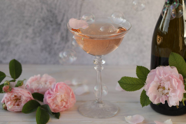 Glass of pink champagne with rose flowers on the light grey background with bubbles - Photo, Image