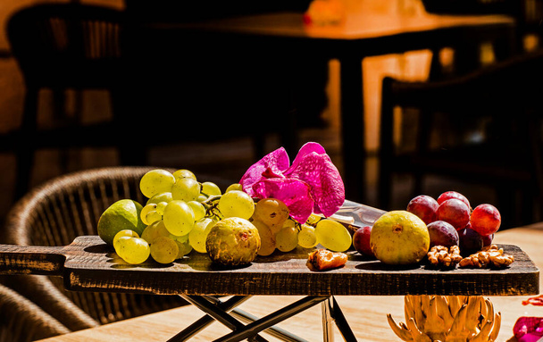 зеленые фрукты и голубой виноград, грецкие орехи и инжир на деревянной доске в кафе снаружи - Фото, изображение