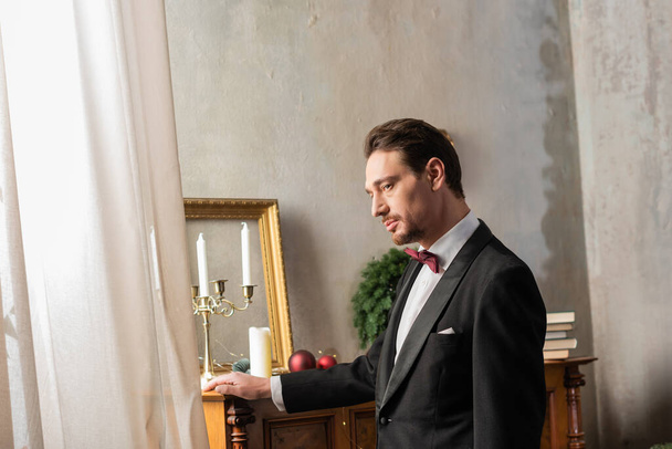 elegancki dżentelmen w formalnym stroju z muszką stojący przy fortepianie w Wigilię Bożego Narodzenia, święto - Zdjęcie, obraz