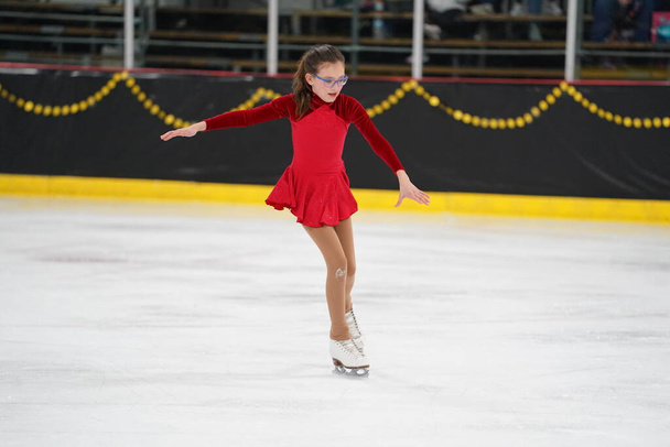 Mosinee, Wisconsin USA - February 26th, 2021: Young adult female in a beautiful red dress participated in badger state winter games ice skating competition. - Photo, Image