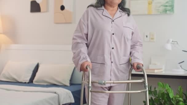 Inclinado retrato de la triste mujer asiática con discapacidad caminando por la habitación con los caminantes, mirando a la cámara - Metraje, vídeo