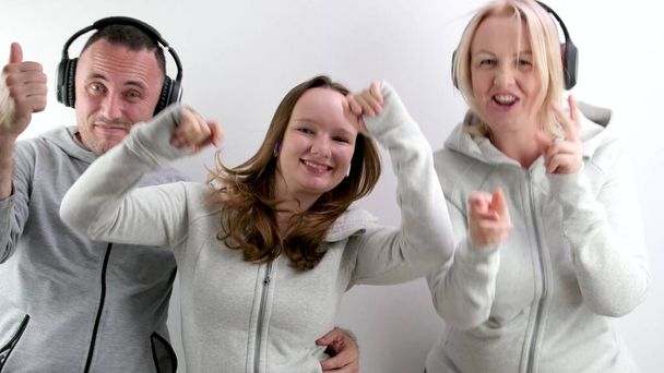 cheerful family in headphones dancing showing thumbs up against the background of white tracksuits having fun family sports spending time together Happy family mom daughter father. cheerful music - Photo, Image