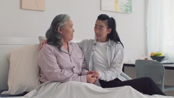 Medium portret shot van zieke senior moeder en haar jonge dochter knuffelen elkaar en kijken naar camera - Video