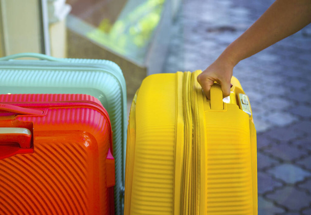 El, sapı için bir bavul tutuyor. Yolculuk için bavullar. Renkli çantalar. Konsept hareket, seyahat, seyahat, uçuş. Yaz tatili kavramı, tatiller. Seyahat için bavul seçiyorum. Bagaj taşıyıcısını al. - Fotoğraf, Görsel