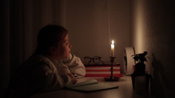 電気のない完全な暗闇の中で自宅で女子高生の距離学習。十代の子供は停電の間彼女の学校の宿題をするためにキャンドルライトを使用する。エネルギー危機の概念。ウクライナの停電. - 映像、動画