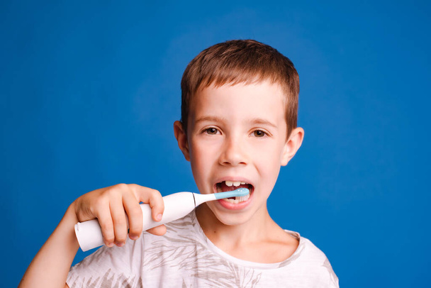 headshot bambino ragazzo tenendo spazzolino e spazzolino da denti con spazzolino elettrico su sfondo studio azzurro - Foto, immagini