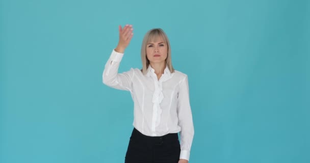 Serious Caucasian woman closing her eyes with her palm on a serene blue background. Her stern expression and the gesture of covering her eyes suggest a moment of introspection or privacy. - Footage, Video
