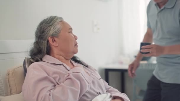 Mediana toma de marido mayor dando a su esposa enferma taza de té caliente mientras cuida de ella en casa - Metraje, vídeo