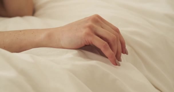 Ezen a közeli felvételen egy nő kezét látjuk, amint gyengéden átsiklik az ágyneműn. Ujjai kedvesen érintik a szövetet, kényelmes és kényelmes érzést keltve.. - Felvétel, videó