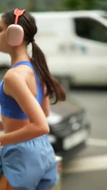 Una giovane donna in abbigliamento sportivo e cuffie sta correndo per le strade della città. Filmati 4k di alta qualità - Filmati, video