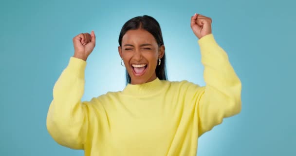 Woman, smile and success with fist in studio to celebrate deal, promotion and winning lotto prize on blue background. Excited indian model shout for celebration, bonus and pride of competition winner. - Footage, Video