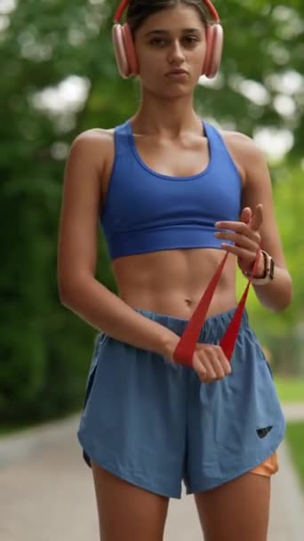 A sportruházatában egy fiatal hölgy fitneszkarkötőt épít be a bemelegítésébe futás előtt. Kiváló minőségű 4k felvételek - Felvétel, videó
