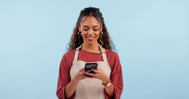 Cafe waitress, woman and phone for business communication, social media post and networking in studio. African entrepreneur, seller or barista for funny meme, mobile chat or typing on blue background. - Footage, Video