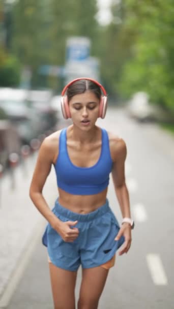 Po bieganiu po ulicach miasta, młoda sportowa dziewczyna w słuchawkach jest wyczerpana. Wysokiej jakości materiał 4k - Materiał filmowy, wideo