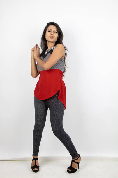 白い背景に赤と灰色のデザイナーの上と黒のジーンズを身に着けているカジュアルな着用で,若く美しいインドの女性モデルのスタジオ撮影. 女性モデル。 ファッション ポートレイト. - 写真・画像