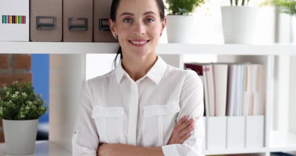Mujer empresaria exitosa sonríe con los brazos cruzados en la oficina de la compañía. Concepto de trabajador posando contra estantes en el lugar de trabajo cámara lenta - Metraje, vídeo