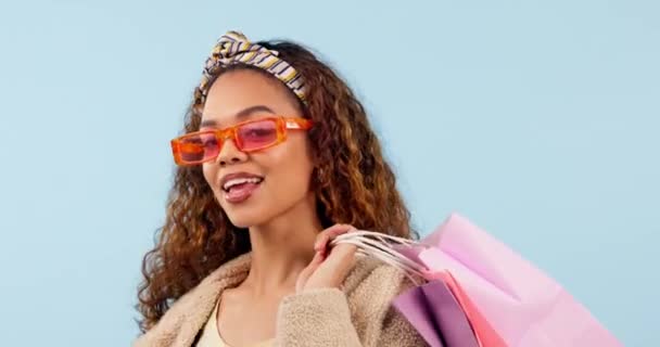 Sluneční brýle, obličej nebo šťastná žena s nákupní taškou ve studiu na prodej nebo propagaci na modrém pozadí. Cool, módní nebo vzrušený gen z zákazník s maloobchodními produkty na slevu nebo nabídku ve studiu. - Záběry, video