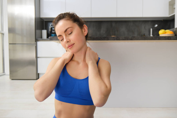 Porträt einer Frau, die von zu Hause aus trainiert, Trainingsübungen macht, ihren Nacken streckt, sich vor der Fitness aufwärmt. Sport- und Wohlfühlkonzept - Foto, Bild