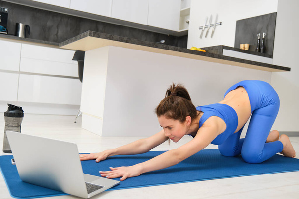 Beeld van jonge sportvrouw, fitness meisje kijken online yoga tutorial op laptop en oefenen, volgende video-instructies. - Foto, afbeelding