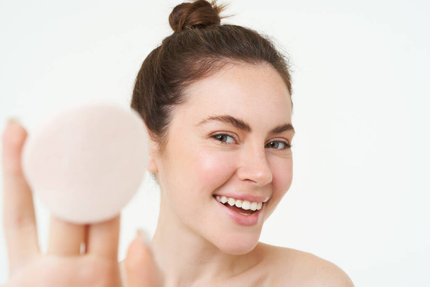 Portrait de beauté d'une jeune mannequin féminine, montrant un coussin de maquillage cosmétique après s'être lavée le visage, à l'aide d'un toner facial, d'un soin de la peau, debout sur un fond blanc. - Photo, image