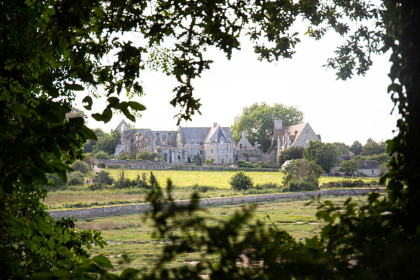 Abadía de Beauport, ubicada en Paimpol, Bretaña, Francia, vista desde una distancia enmarcada con hojas. - Foto, Imagen