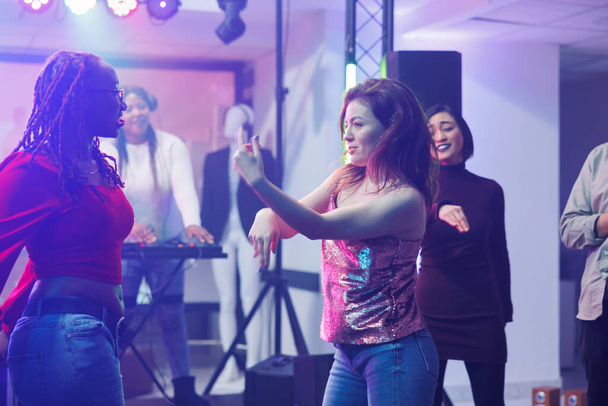 Energetic women dancers improvising moves while clubbing and enjoying nightlife leisure activity. Girlfriends doing dance battle on dancefloor at discotheque party in nightclub - Photo, Image