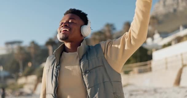 Headphones, music and black man dance at beach for freedom on holiday outdoor. Happy African person listening to radio, moving and streaming audio, smile for sound or hearing media on summer vacation. - Footage, Video