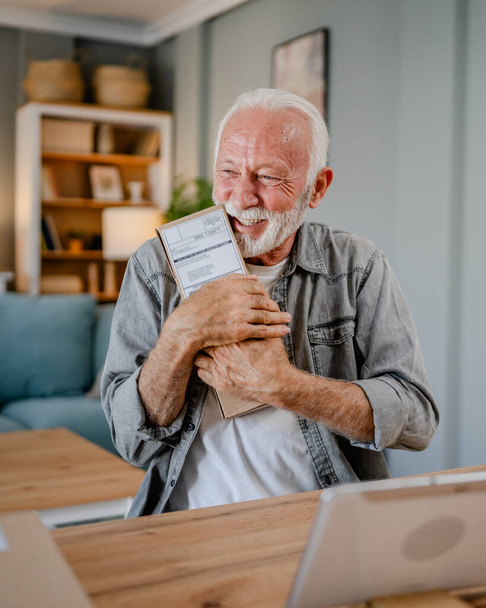 Un hombre caucásico senior en casa sostiene el paquete de la caja de cartón entregado regalo u orden - Foto, Imagen