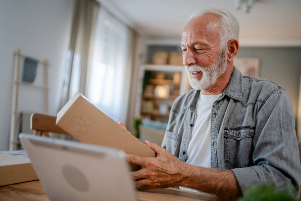 Un hombre caucásico senior en casa sostiene el paquete de la caja de cartón entregado regalo u orden - Foto, Imagen