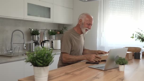 Un homme caucasien senior à la maison tenir paquet cardbox livré cadeau ou une commande utiliser ordinateur portable en ligne pour vérifier l'état des achats expédition ou pour l'espace de copie d'appel vidéo - Séquence, vidéo
