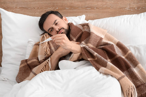 Nemocný mladý muž s teploměrem ležícím v posteli - Fotografie, Obrázek