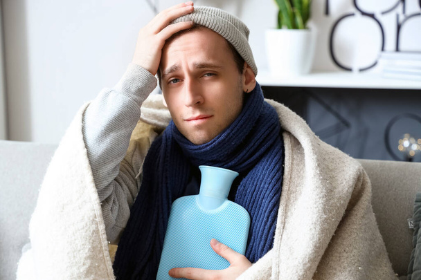 Ill young man with hot water bottle at home, closeup - Photo, Image