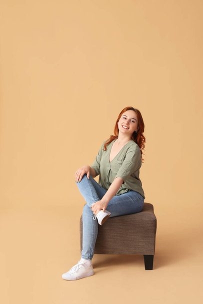 Young woman sitting on pouf against beige background - Photo, Image