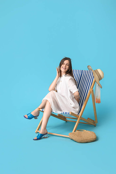 Νεαρή γυναίκα χαλαρώνει στο κατάστρωμα καρέκλα σε μπλε φόντο - Φωτογραφία, εικόνα