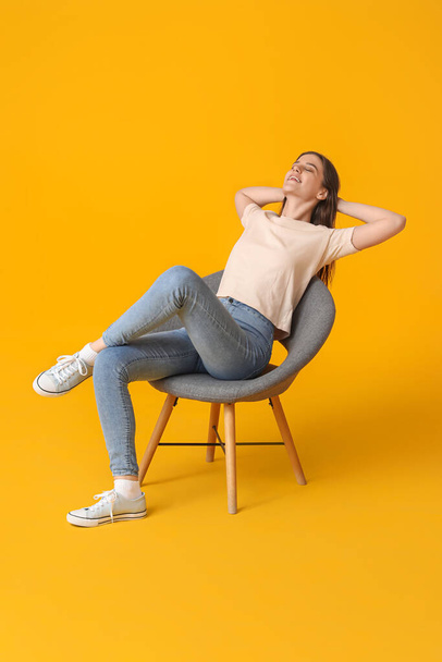 黄色い背景に椅子に座っている若い女性 - 写真・画像