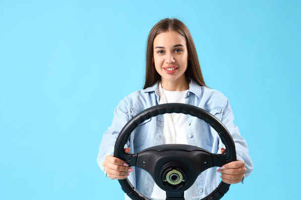Jonge vrouw met stuurwiel op blauwe achtergrond - Foto, afbeelding