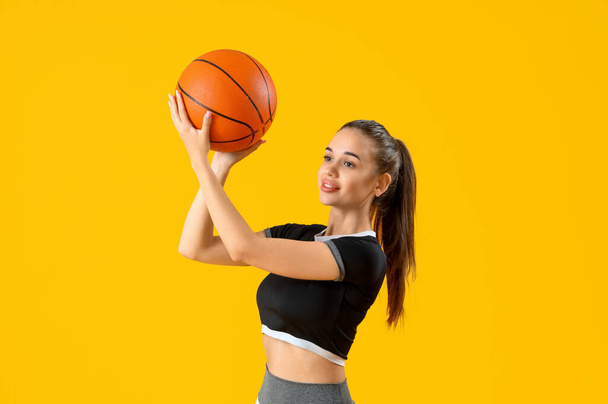 Mujer joven deportiva con pelota sobre fondo amarillo - Foto, Imagen