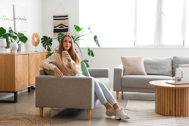 Fiatal nő csésze kávéval ül a kanapén a nappaliban - Fotó, kép