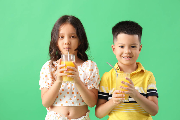 緑の背景に新鮮な柑橘類ジュースのグラスを持つ小さなアジアの子供たち - 写真・画像