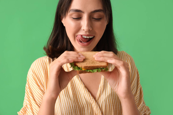 Красива молода жінка зі смачним бутербродом на зеленому фоні - Фото, зображення