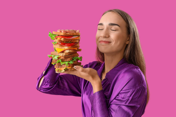 Όμορφη νεαρή γυναίκα με μεγάλο σάντουιτς σε μωβ φόντο - Φωτογραφία, εικόνα