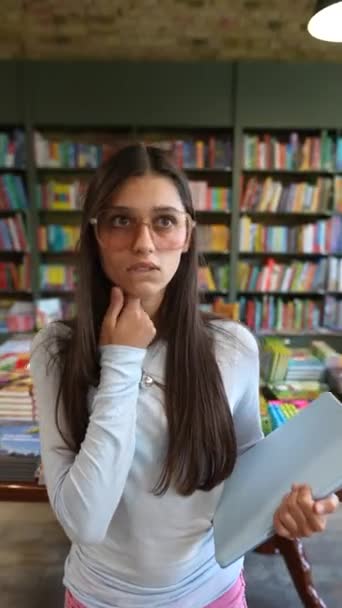 Uma jovem linda explica a livraria com um tablet nas mãos. Imagens 4k de alta qualidade - Filmagem, Vídeo