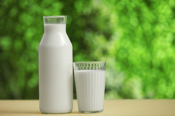 Vidrio y botella de leche fresca en la mesa de madera amarilla al aire libre - Foto, imagen