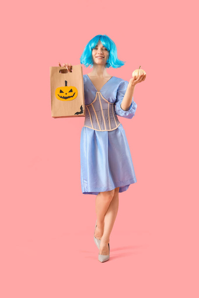 Young woman dressed for Halloween with gift bag and pumpkin on pink background - Photo, Image