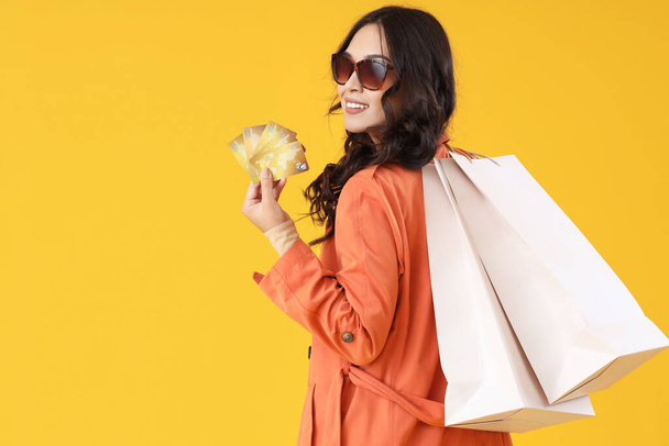 Young Asian woman with credit cards and shopping bags on yellow background - Photo, Image