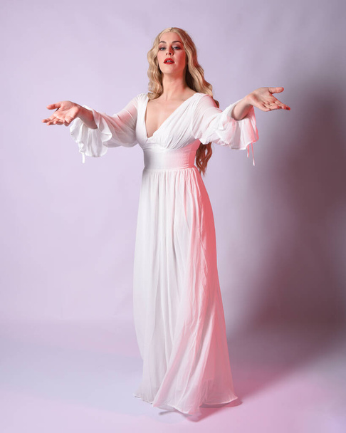Full length portrait  of blonde woman  wearing white historical bridal gown fantasy costume dress.    Standing pose, facing forwards with gestural arms reaching out , isolated on studio background. - Photo, Image